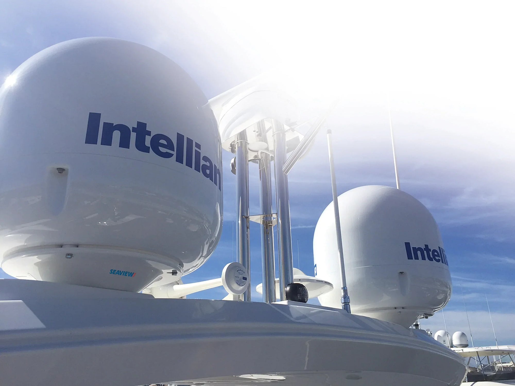 Low-profile adapters on a yacht with Intellian satellite domes against a blue sky.